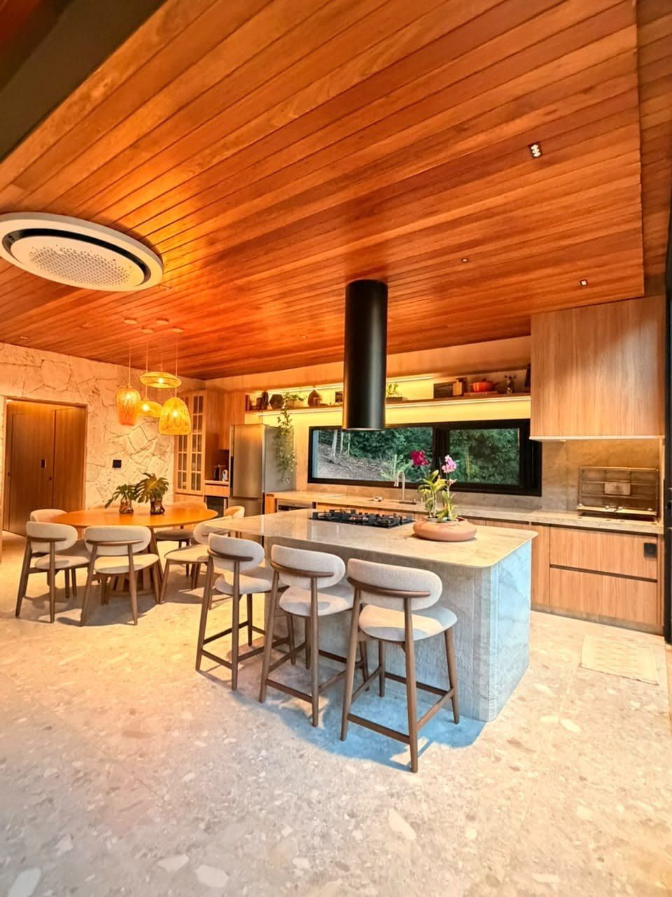 Cozinha com ilha em pedra, cooktop, coifa e bancos altos