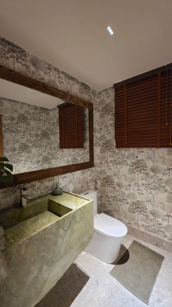 Lavabo com cuba esculpida em pedra verde e papel de parede botânico