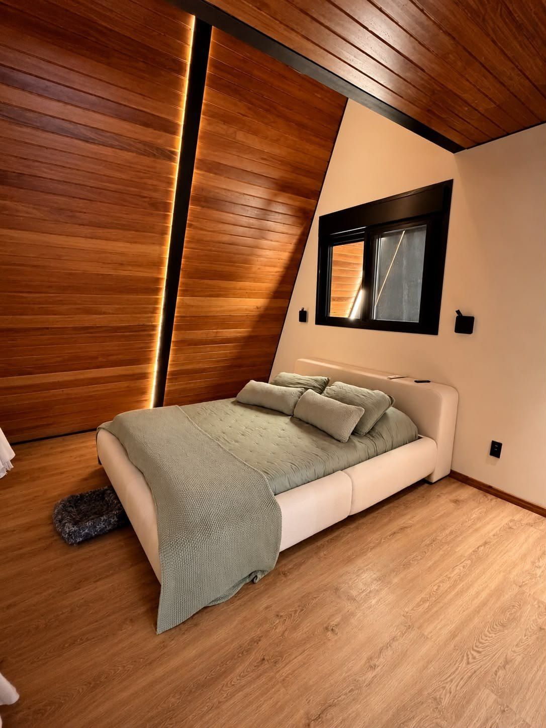 Cama de casal sob o forro inclinado de madeira, com roupa de cama em verde-sálvia